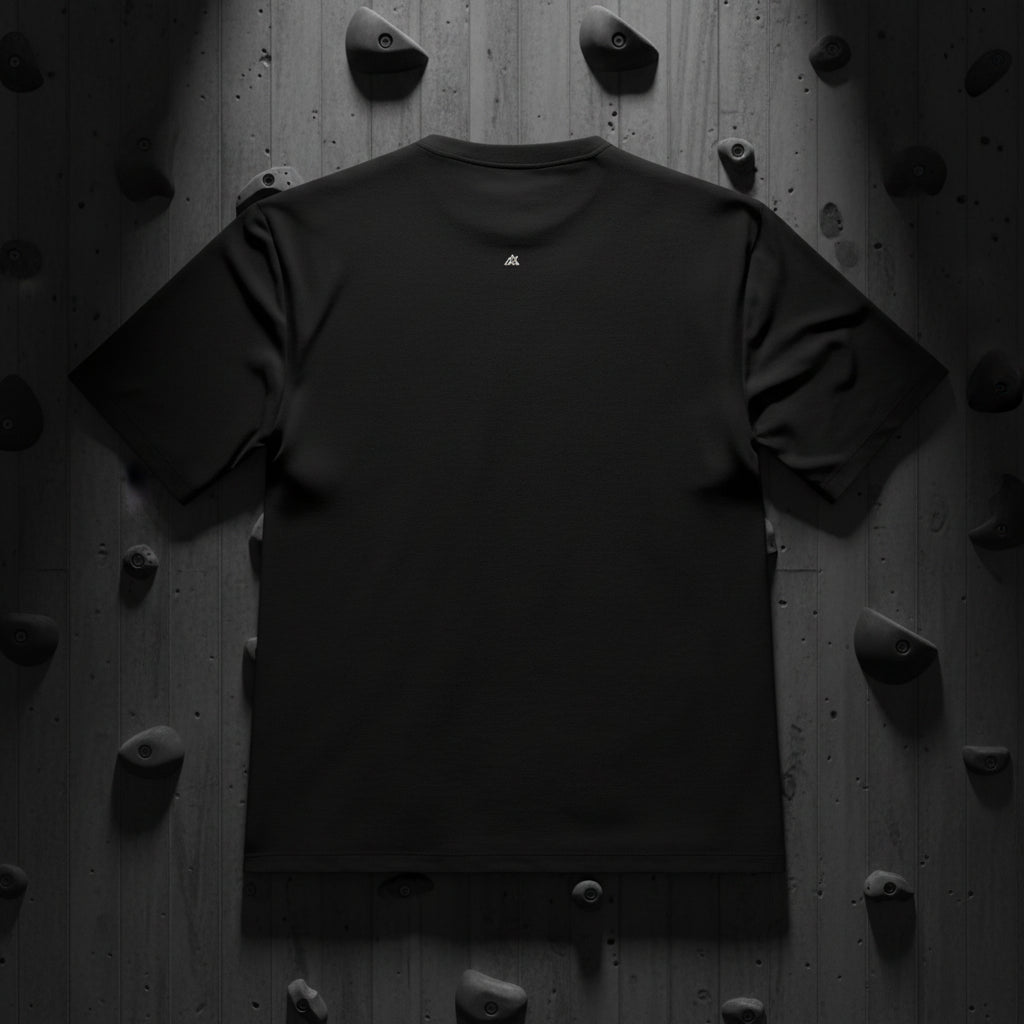 Vista trasera de modelo fitness con la camiseta Core Gravity, mostrando el logo minimalista en la nuca. Fondo de muro de escalada de hormigón texturizado oscuro con iluminación tenue