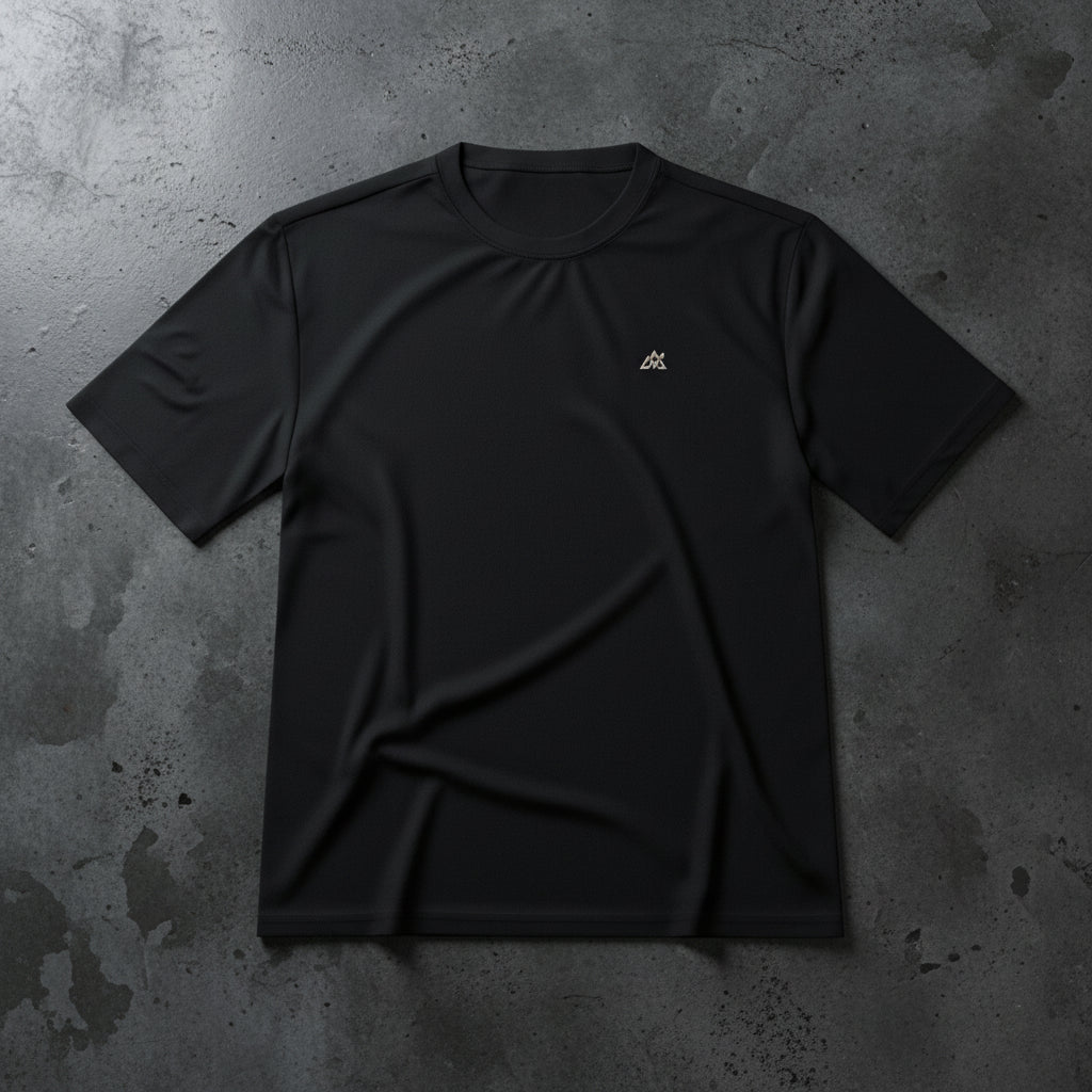 Camiseta técnica Core Gravity Tech-Shell color Iron Black en toma plana sobre una superficie de hormigón pulido oscuro con iluminación dramática de estudio