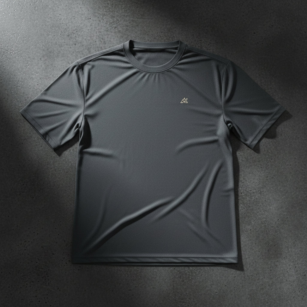 Camiseta técnica Core Gravity Tech-Shell color Iron Black en toma plana sobre una superficie de hormigón pulido oscuro con iluminación dramática de estudio